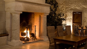 A stone fireplace with a fire, surrounded by wicker furniture and a wooden table. - Château Latour Segur Suites & Spa (Lussac)
