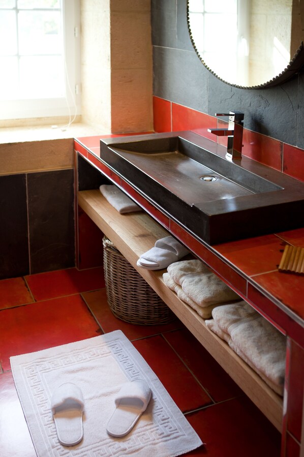 A bathroom with a wooden vanity, a sink, a mirror, and a red tiled floor.