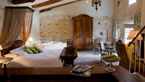 A room with a bed, a wooden table, a chandelier, a wooden cabinet, and a bathroom with a bathtub. - Château Latour Segur Suites & Spa (Lussac)