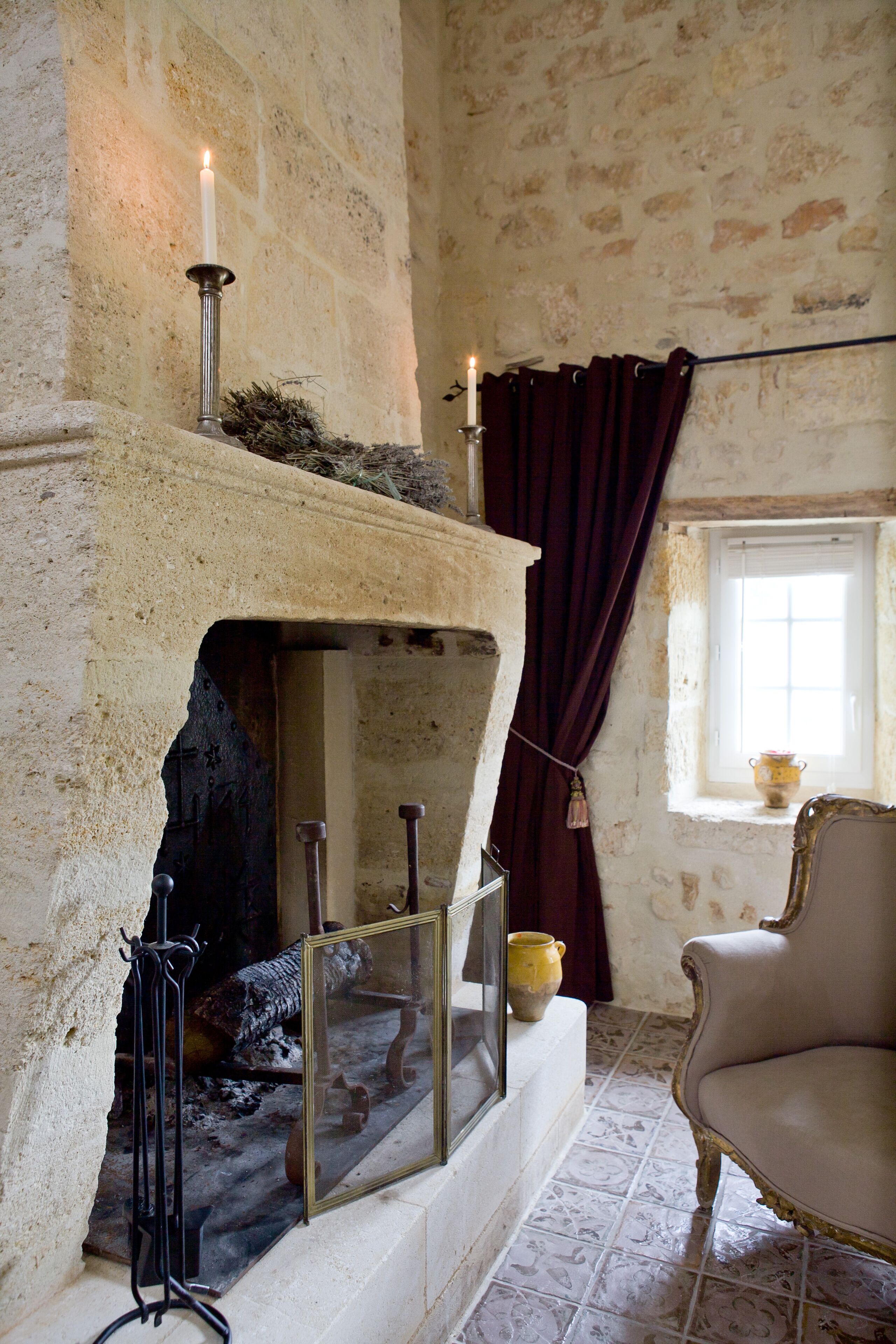 A room with a stone fireplace, a chair, and a window with curtains.