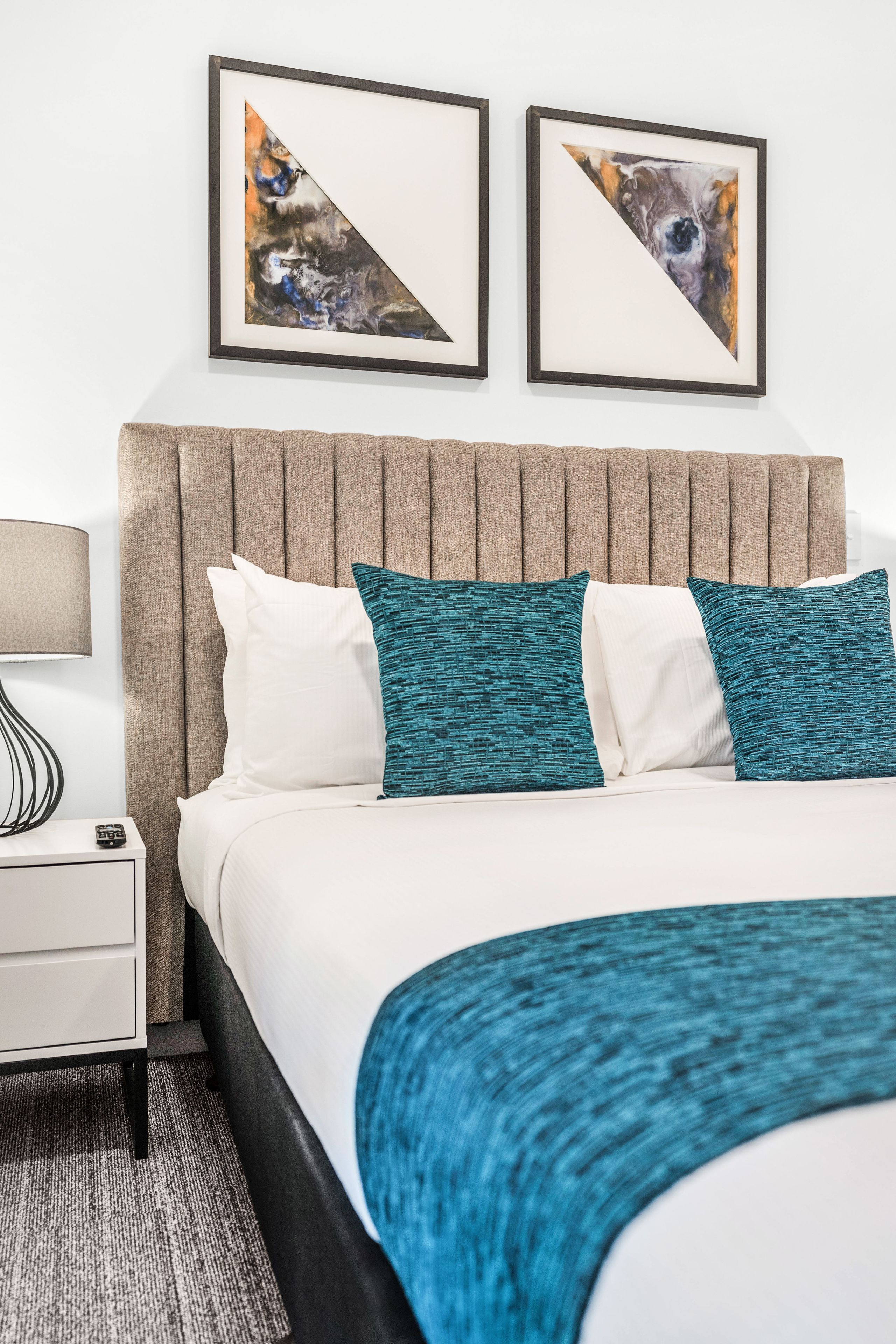 A hotel room with a bed, a nightstand, a lamp, and two framed pictures on the wall.