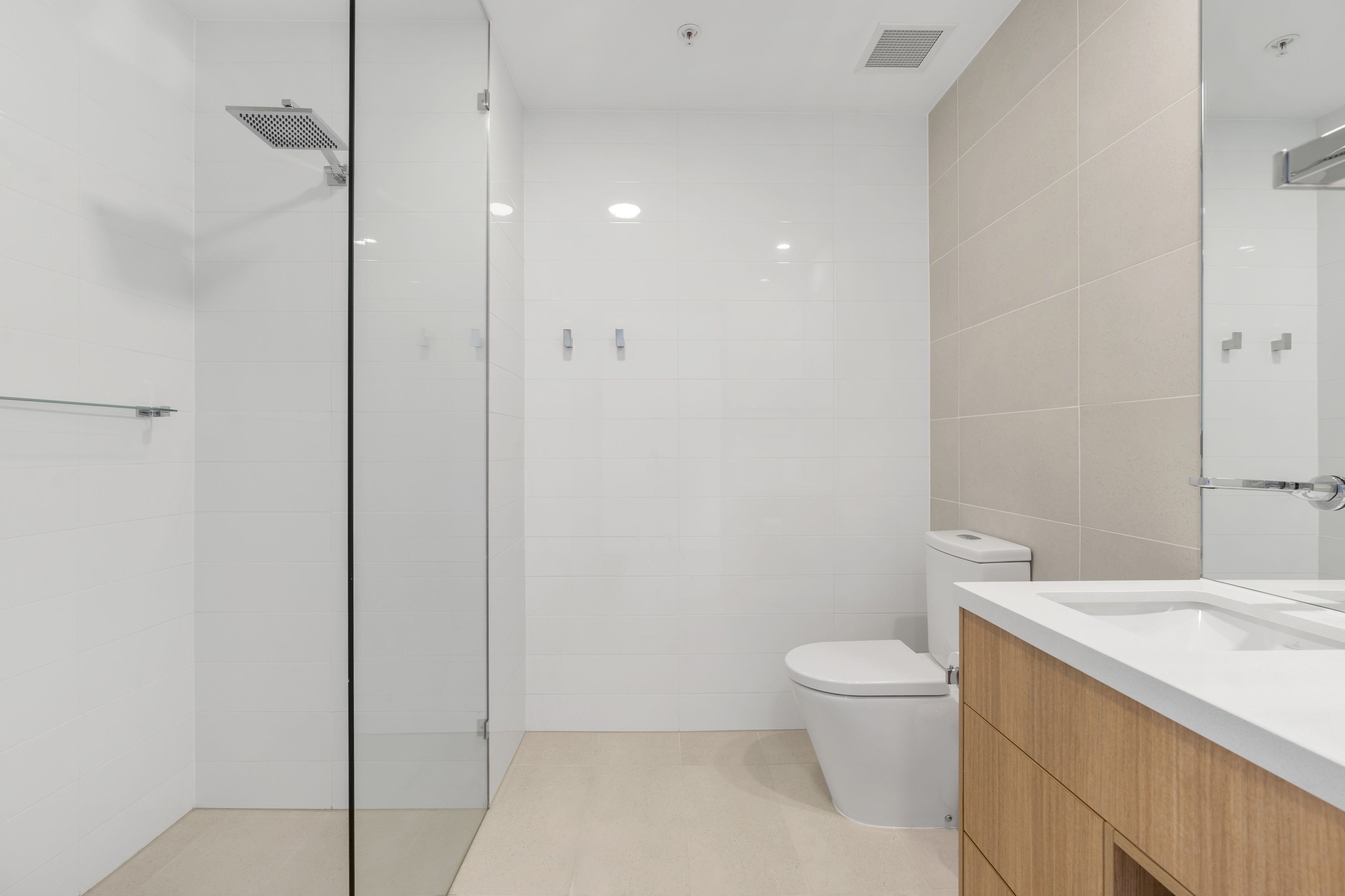 A modern bathroom with a glass shower enclosure, a white toilet, and a wooden vanity with a mirror.