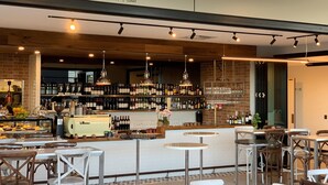 A café with a bar area, wooden tables, and a variety of bottles and glasses on shelves. - Essence Suites Taringa (Taringa)