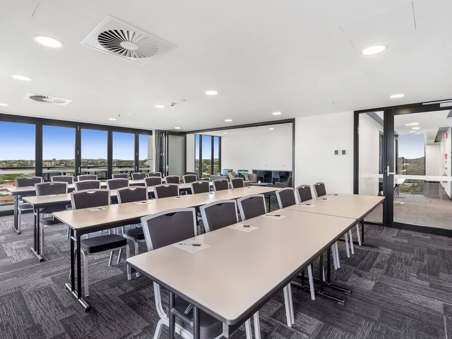 A conference room with large tables and chairs, large windows with a view of the city, and a modern ceiling design.