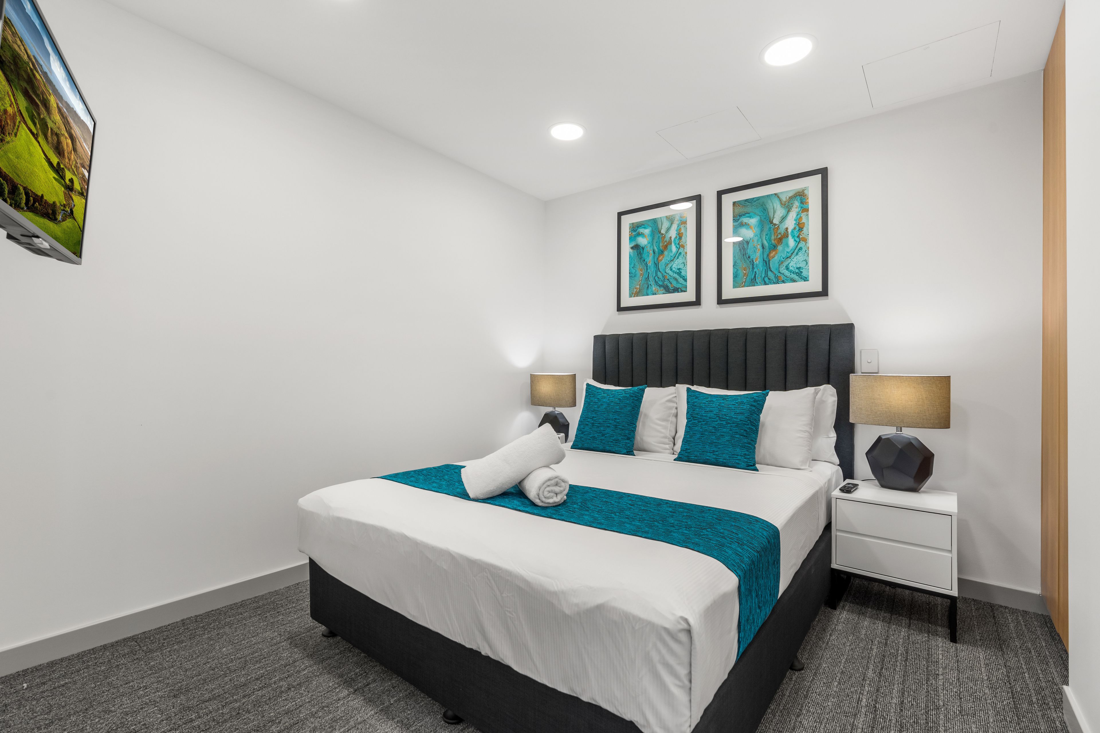 Un hotel moderno con una cama grande, dos mesitas de noche con lámparas y dos cuadros abstractos en la pared.