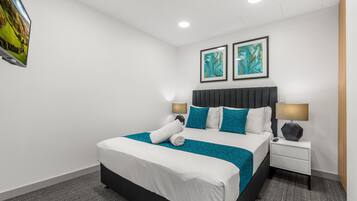 Un hotel moderno con una cama grande, dos mesitas de noche con lámparas y dos cuadros abstractos en la pared.