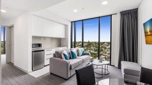 A modern living room with a grey sofa, a dining table, and a kitchen area with white cabinets and a microwave. - Essence Suites Taringa (Taringa)