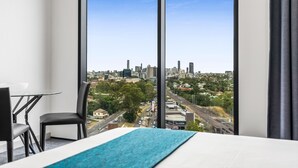 Habitación de hotel con un ventanal grande que ofrece vistas a la ciudad, una cama, una mesita y una silla.