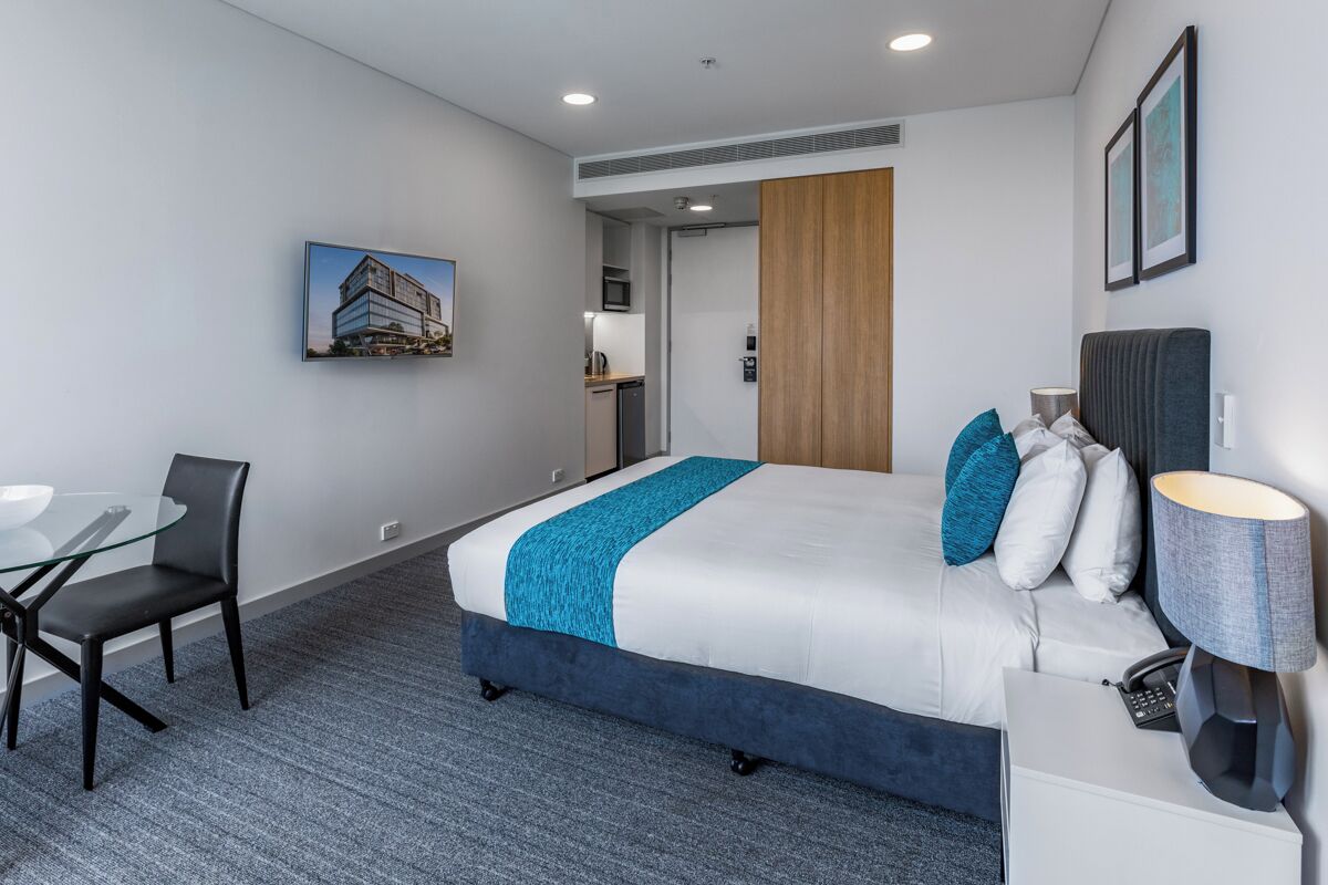 A hotel room with a bed, a desk, a chair, a lamp, and a picture on the wall.