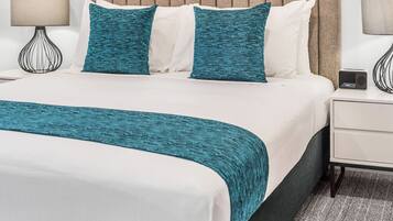 Habitación de hotel con una cama grande, cabecera, dos obras de arte enmarcadas, una mesita de noche con lámpara y una mesita auxiliar.