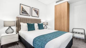 A modern hotel room with a large bed, two bedside tables with lamps, a wooden wardrobe, and two framed pictures on the wall.
