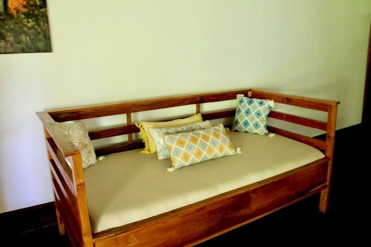Un sofá de madera con un cojín color beige, dos almohadas con un estampado geométrico y una almohada lisa.