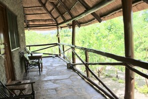 Un espacio al aire libre techado con suelo de piedra, mobiliario de madera y techo de paja.