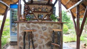 Un bar extérieur de style rustique, avec un mur en pierre, des tabourets en bois et une variété de bouteilles et de verres.