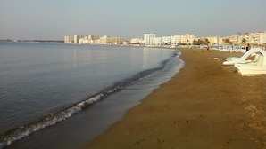 A beach with a row of boats on the right, a calm sea, and buildings in the background. - Jasmin Court Apart Otel (Silifke)