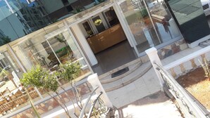 A modern building with a glass facade, a wooden bench, and a small tree. - Jasmin Court Apart Otel (Silifke)