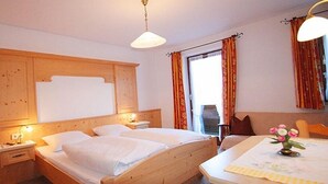 A hotel room with two single beds, wooden headboard, bedside tables with lamps, a window with curtains, and a table with a vase of flowers. - Liebertingerhof (Reit im Winkl)