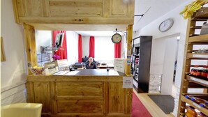 A wooden reception desk with a clock, a counter with a computer, and a shelf with bottles. - Picobello Pension (Görlitz)
