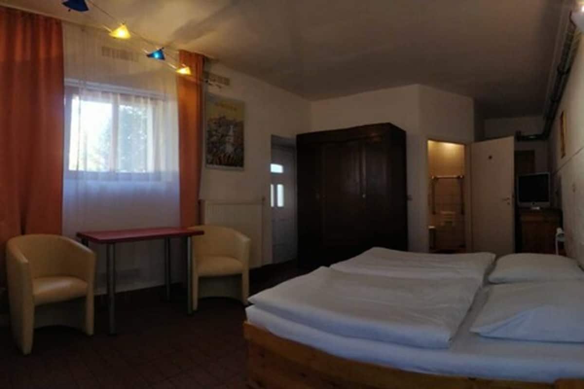 A room with a bed, a desk, two chairs, a wardrobe, and a window with curtains.