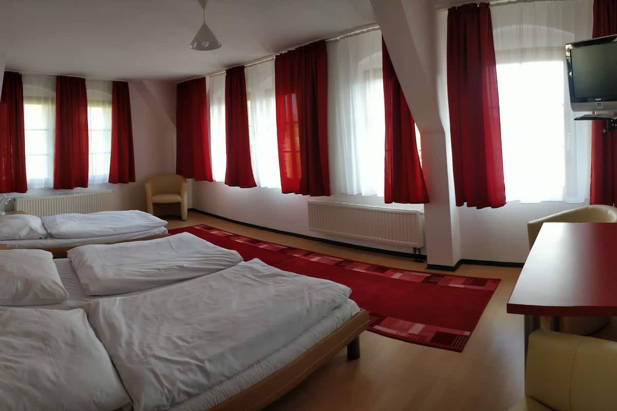 A hotel room with three beds, a red carpet, a TV mounted on the wall, and a red table.