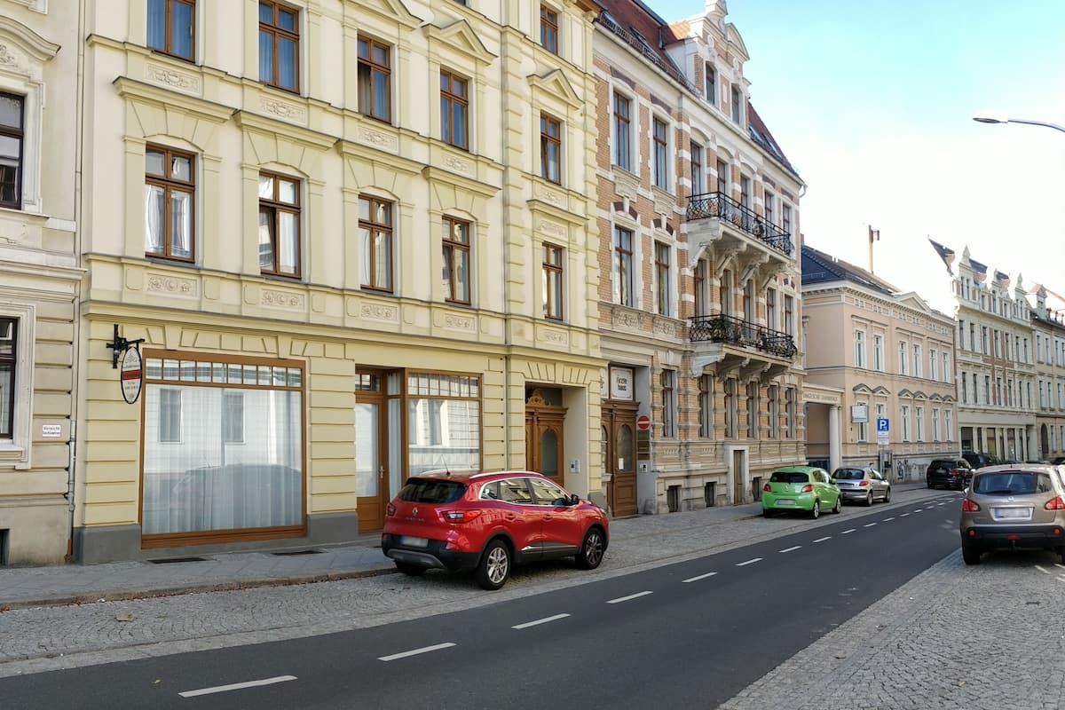 A street with historic buildings, parked cars, and cobblestone pavement.