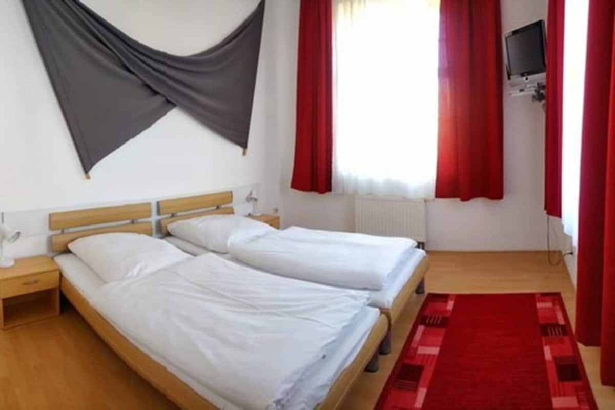 A room with two single beds, a wooden headboard, a nightstand, a red rug, and a TV mounted on the wall.