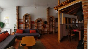 A cozy living room with a sofa, a coffee table, and a TV. There are brick arches and shelves with various items. - Picobello Pension (Görlitz)