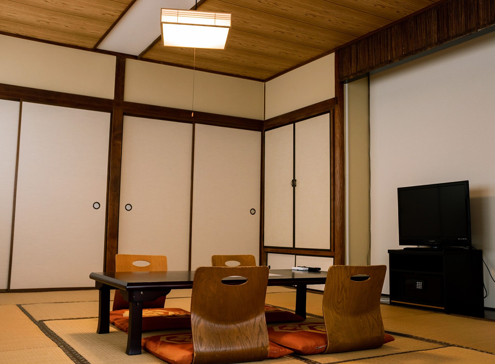 A traditional Japanese room with tatami flooring, a low table, wooden chairs, and a television.
