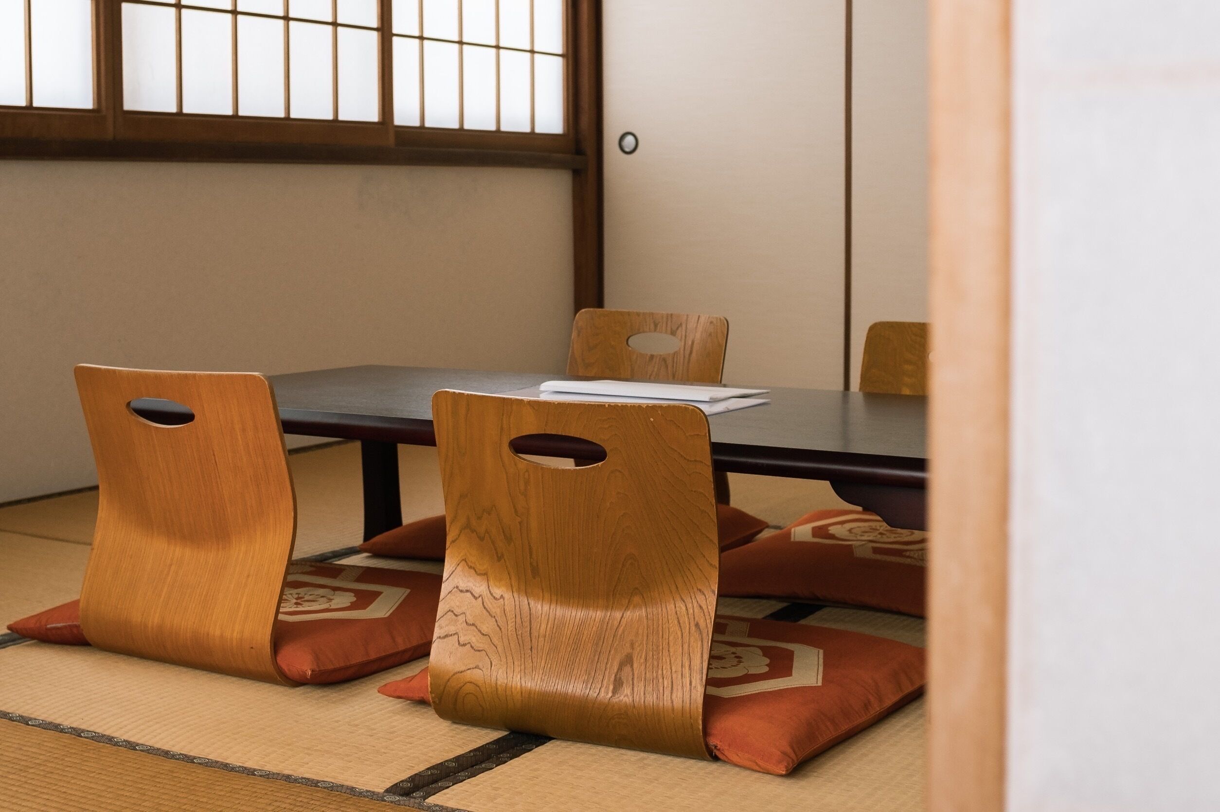 A traditional Japanese room with tatami flooring, a low table, and wooden chairs with cut-out backs.
