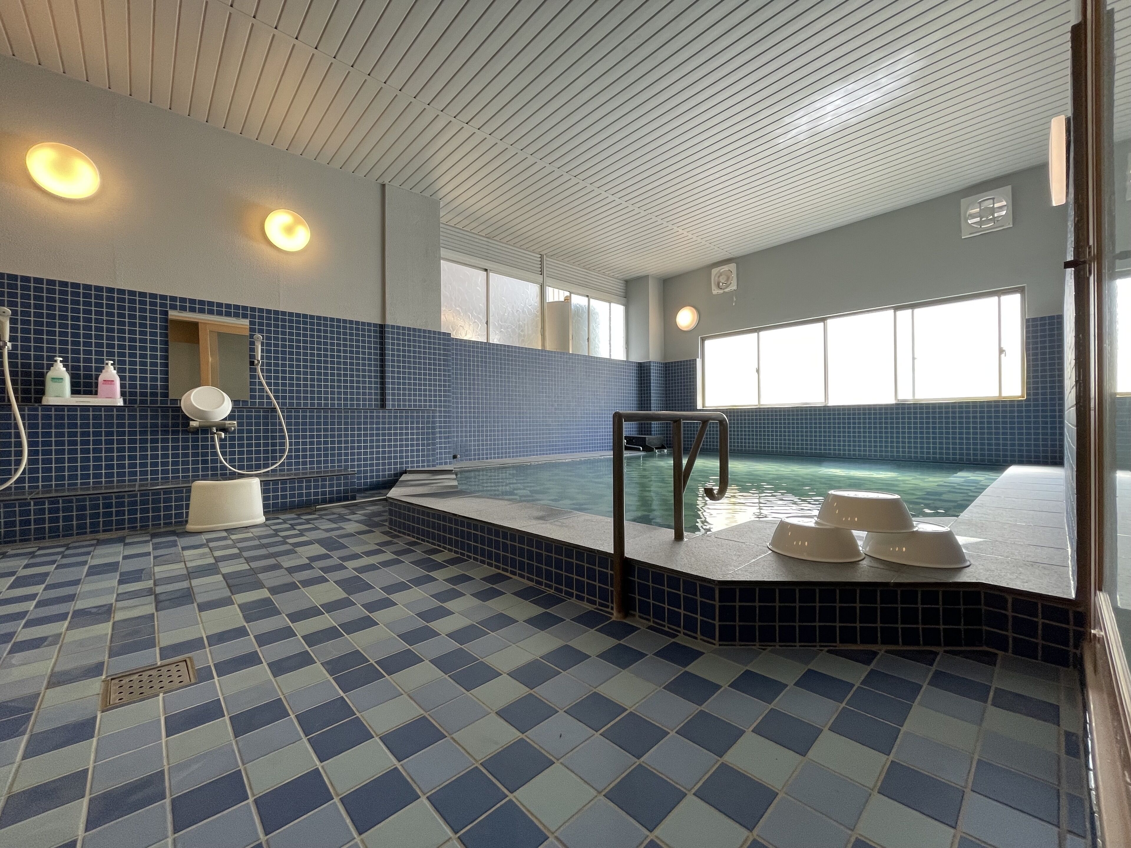 A swimming pool with a checkered floor, a small seating area, and a window providing natural light.