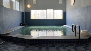 An indoor swimming pool with blue tiled walls and a clear view of the sky through a large window.