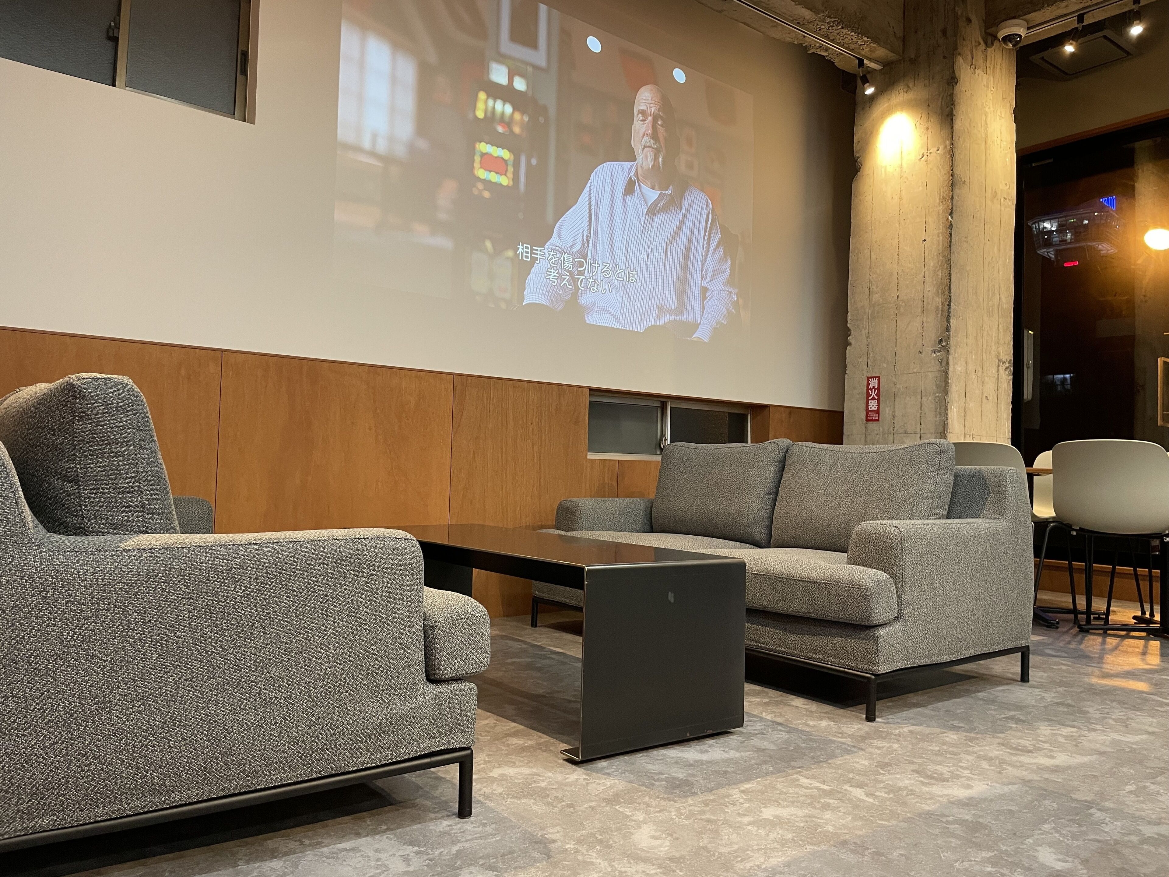A modern conference room with a large screen displaying a presentation, grey upholstered sofas, a small table, and a laptop.