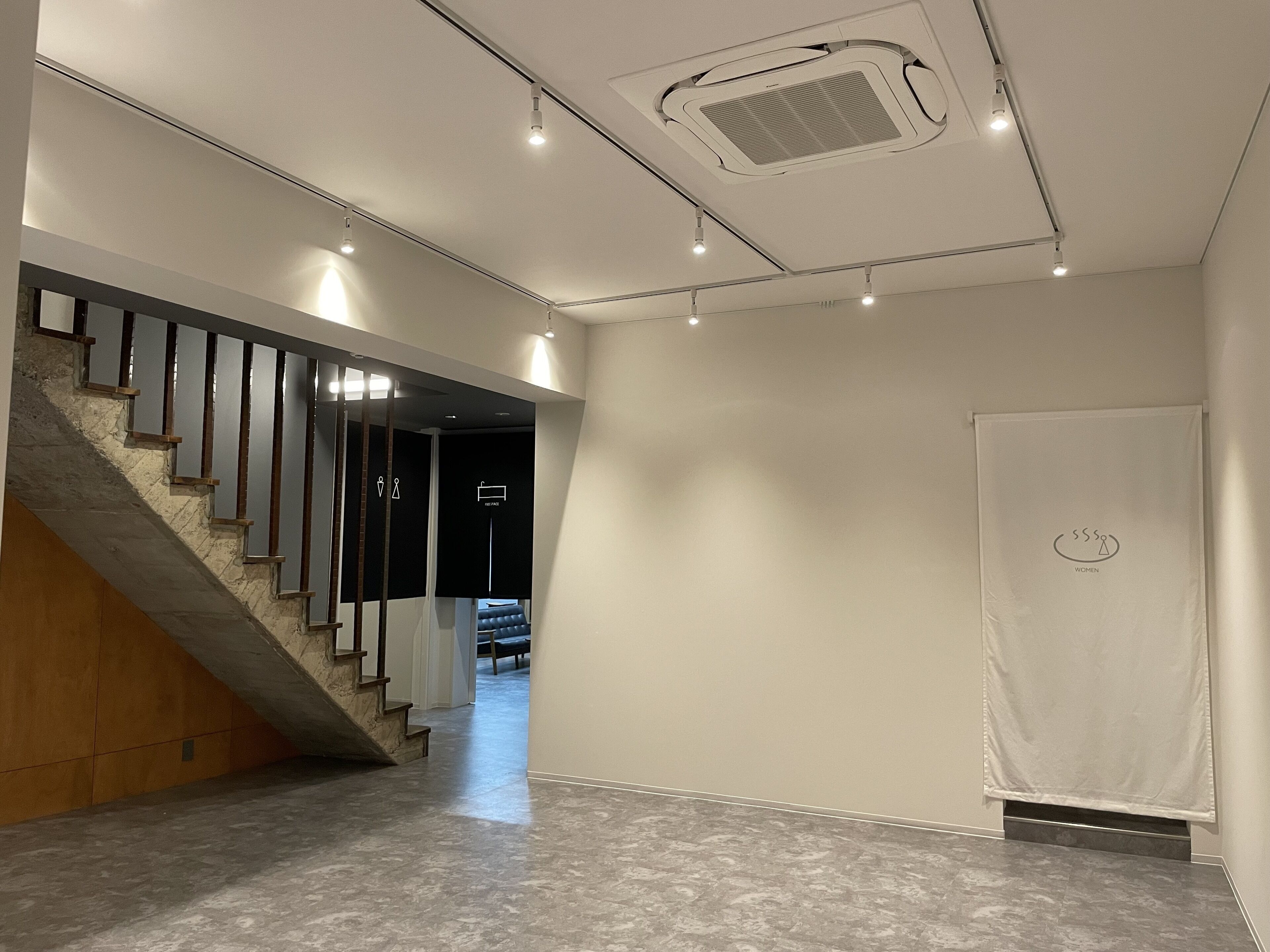A modern interior with a staircase, a ceiling vent, and a plain wall with a curtain.