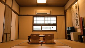 A traditional Japanese room with tatami flooring, a low table with cushions, sliding doors, and a television.