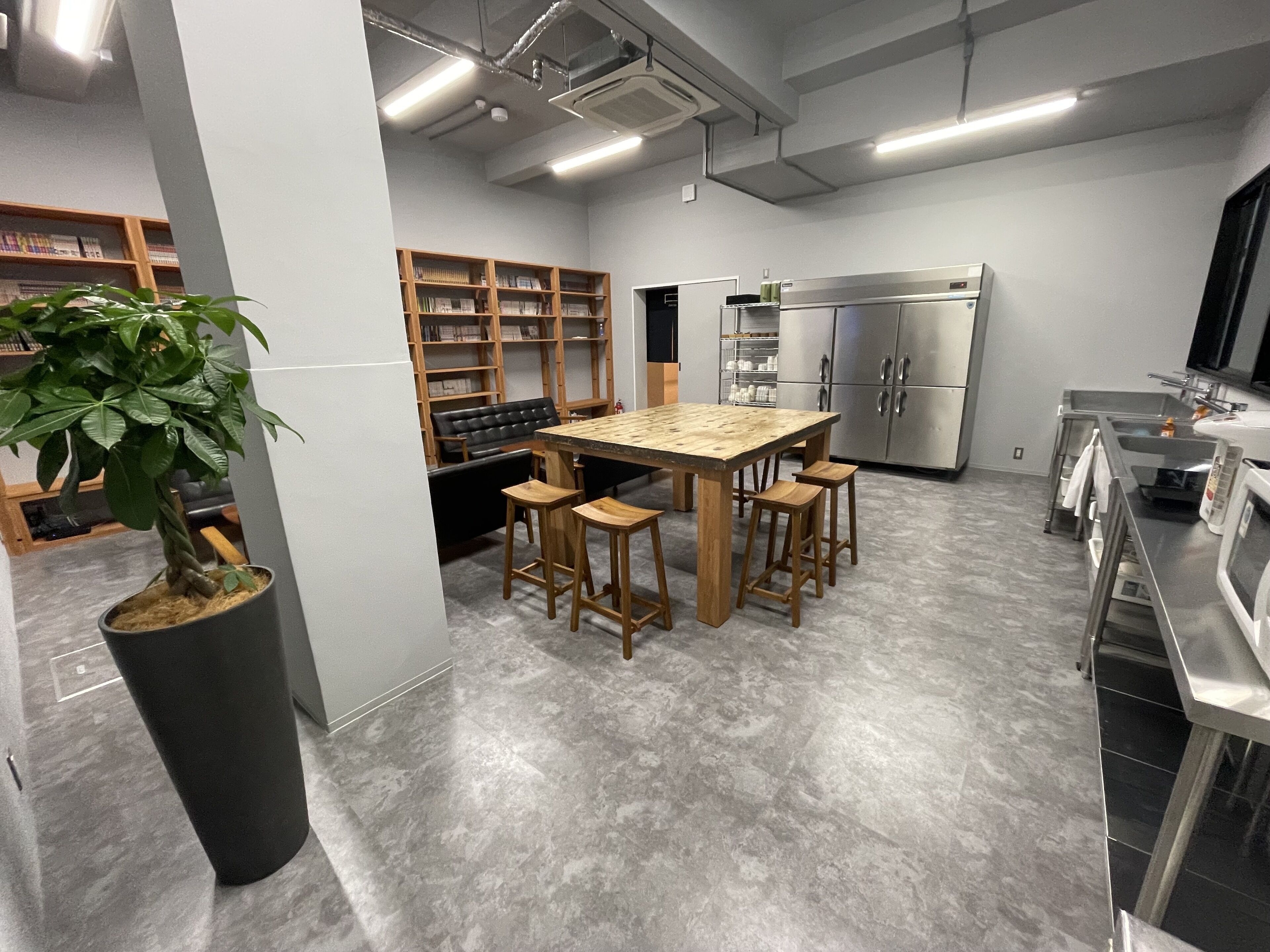 A modern kitchen with a central island, bar stools, a potted plant, and built-in shelving.