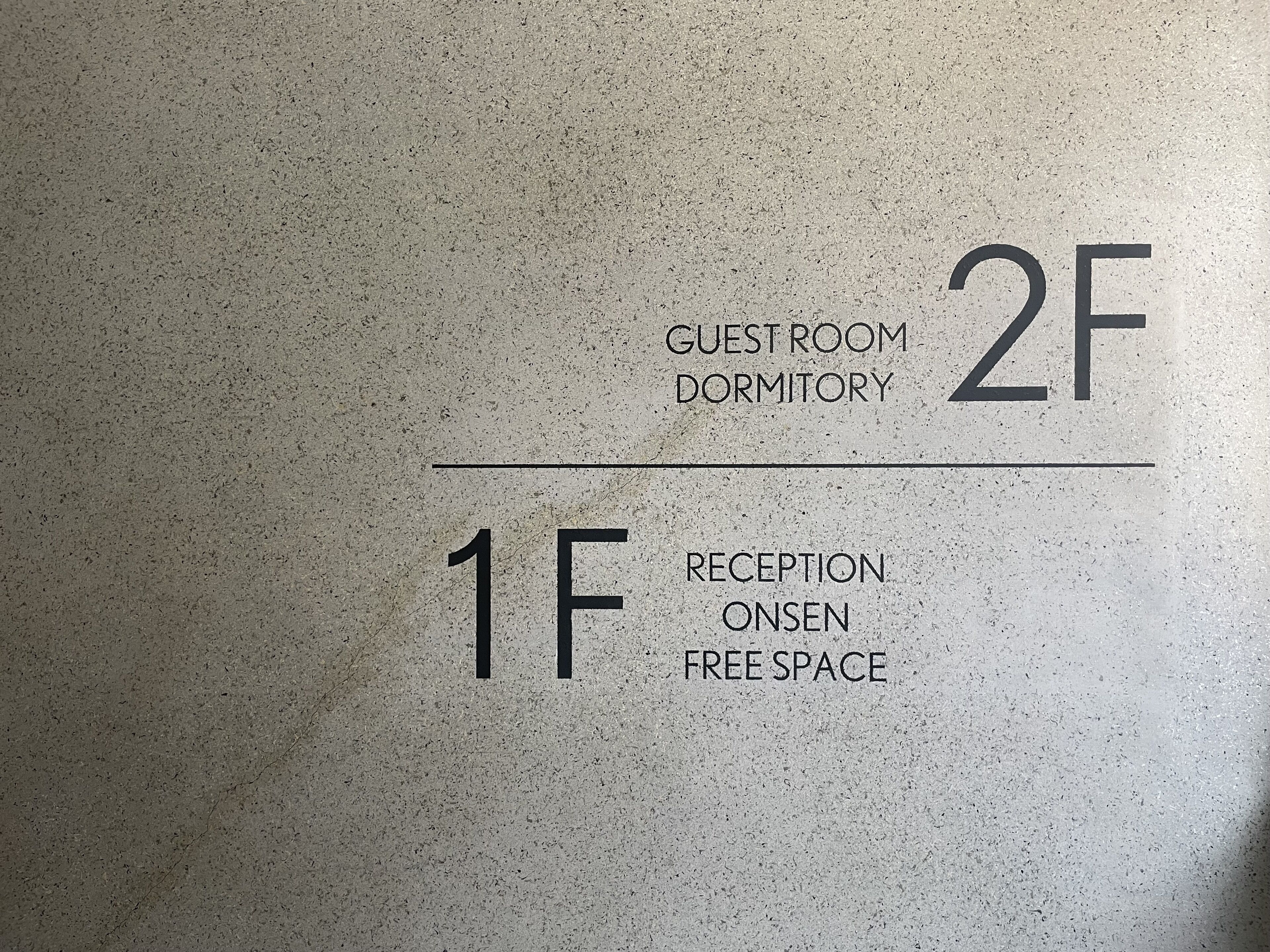 En væg med rumskilte: "1F RECEPTION ONSEN FREE SPACE" og "2F GUEST ROOM DORMITORY".