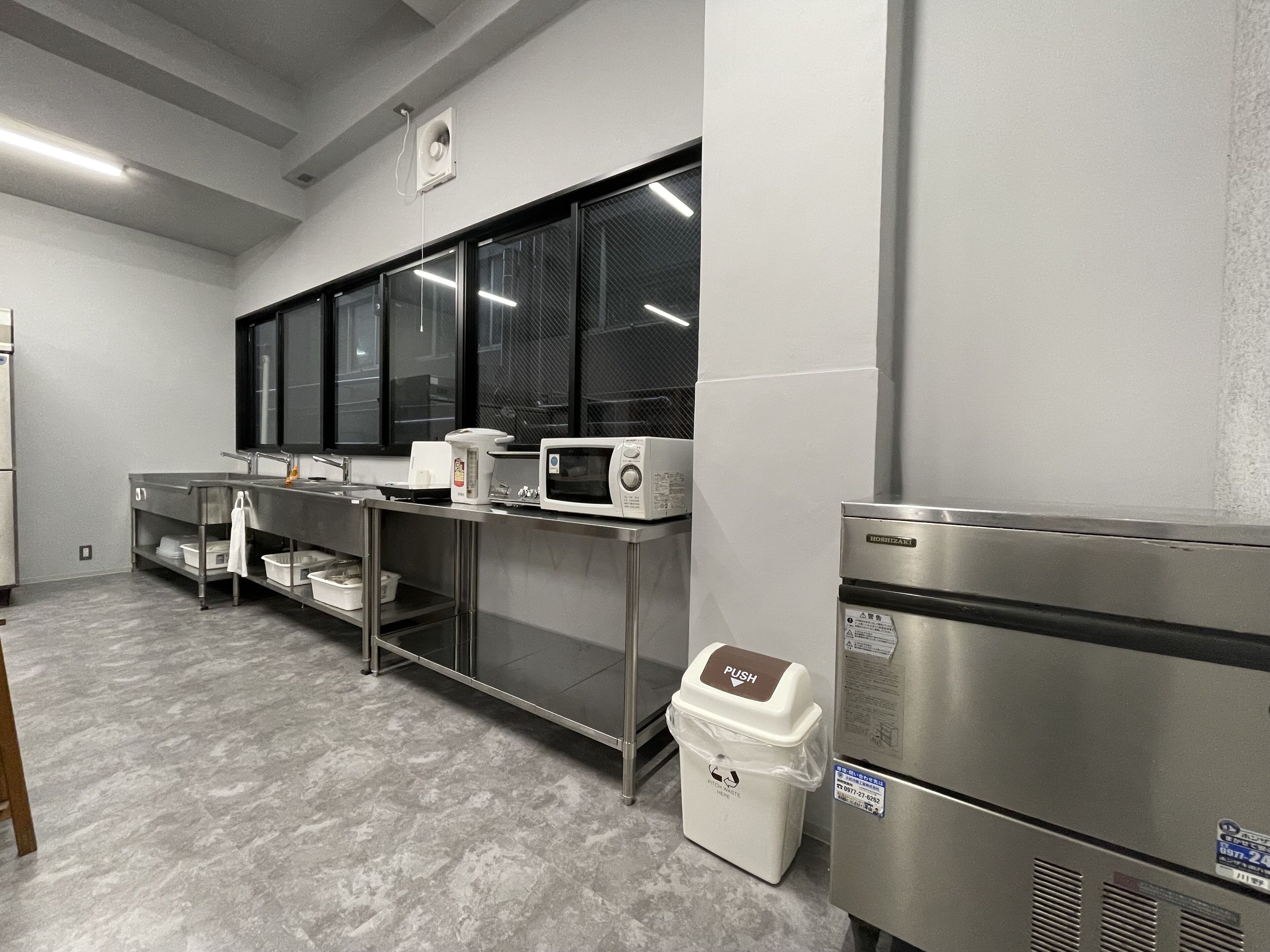 A commercial kitchen with stainless steel appliances, a large window, and a trash bin.
