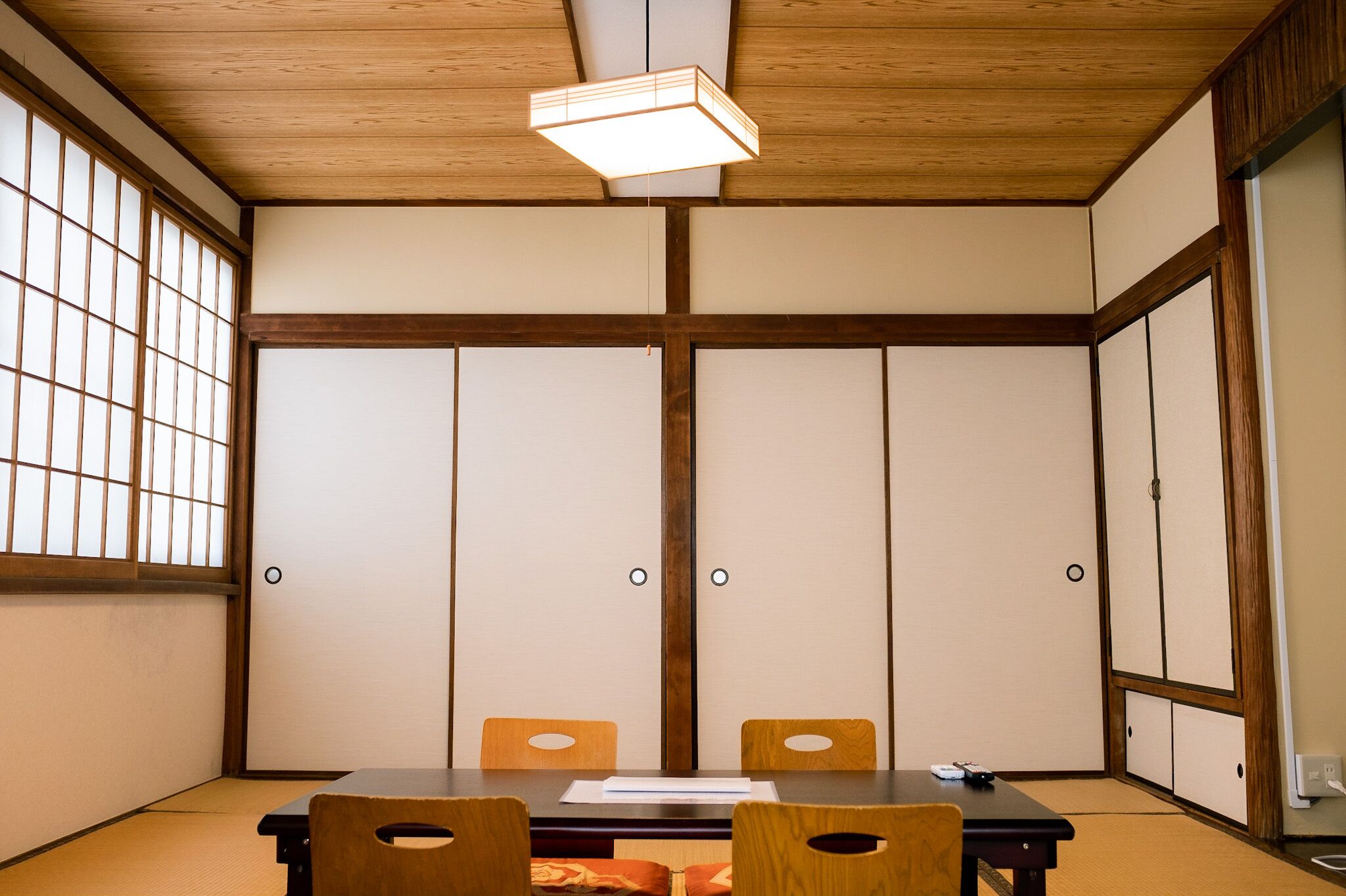 A traditional Japanese room with tatami flooring, a low table with chairs, sliding doors, and a ceiling light fixture.