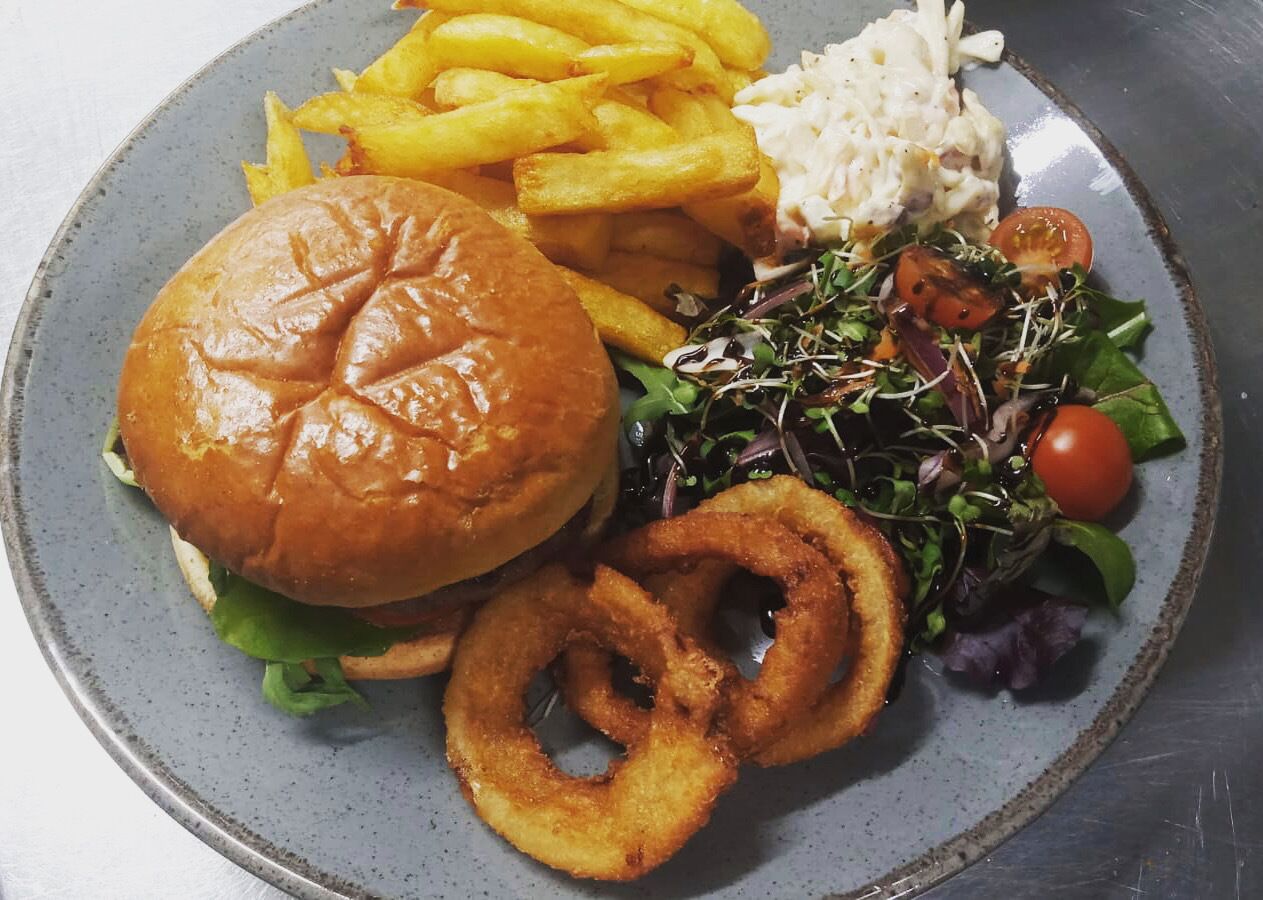 Ein Teller mit einem Burger, Pommes, Zwiebelringen, Krautsalat und einem Salat.