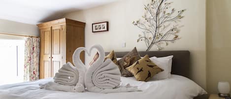 A neatly made bed with white linens, a heart-shaped towel arrangement, and decorative pillows.
