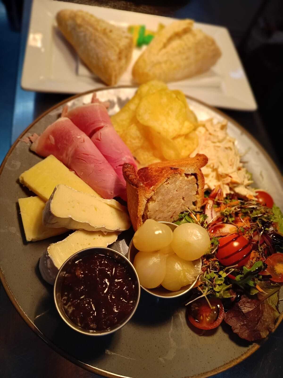 Um prato com diversos queijos, charcutaria, uvas e uma salada.