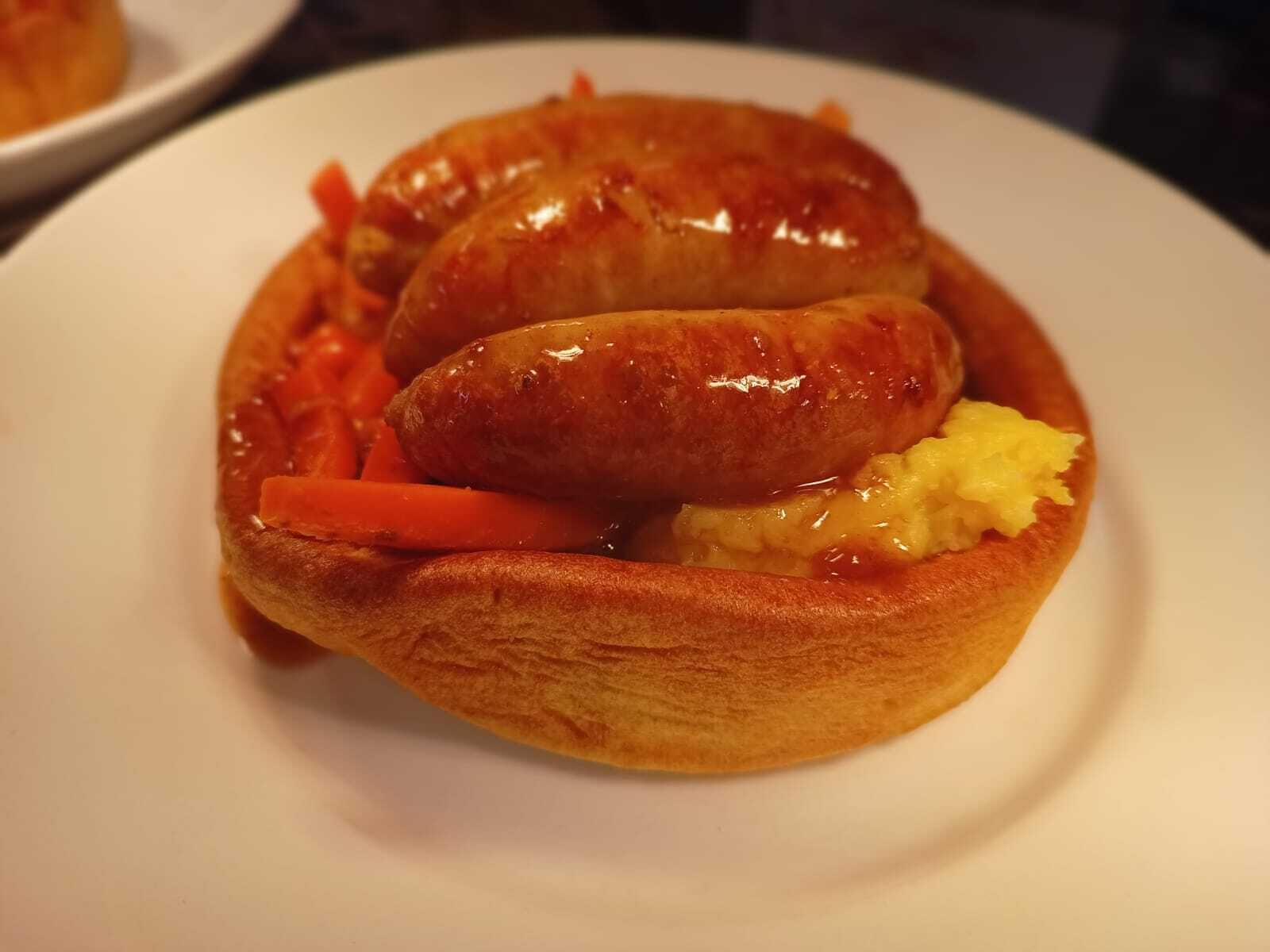 A plate with two sausages, carrots, and pineapple.