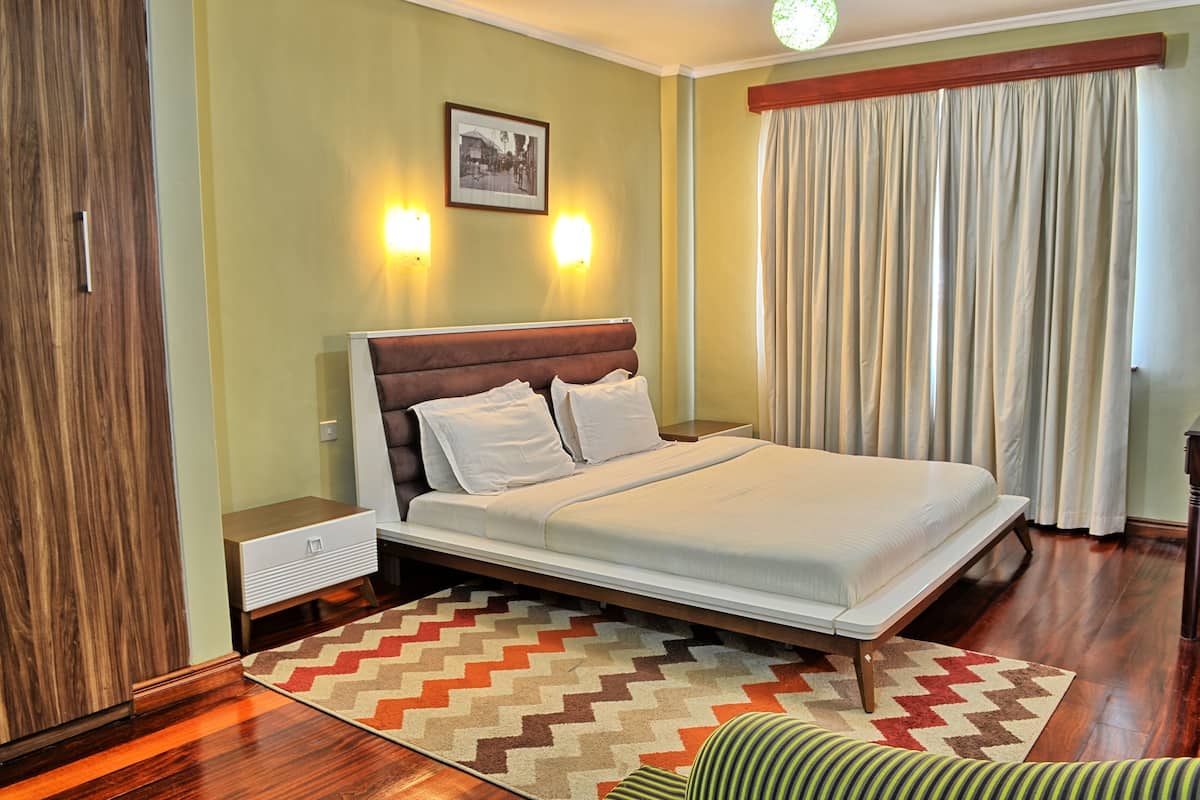 A bedroom with a bed, nightstands, a wall-mounted light, a window with curtains, and a picture on the wall.