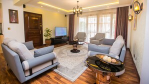A modern living room with a sofa, armchairs, a coffee table, and a TV. - Serene Valley Apartments & Spa (Nairobi)