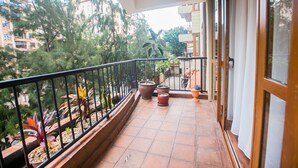 A balcony with potted plants, a tiled floor, and a view of surrounding buildings and trees. - Serene Valley Apartments & Spa (Nairobi)
