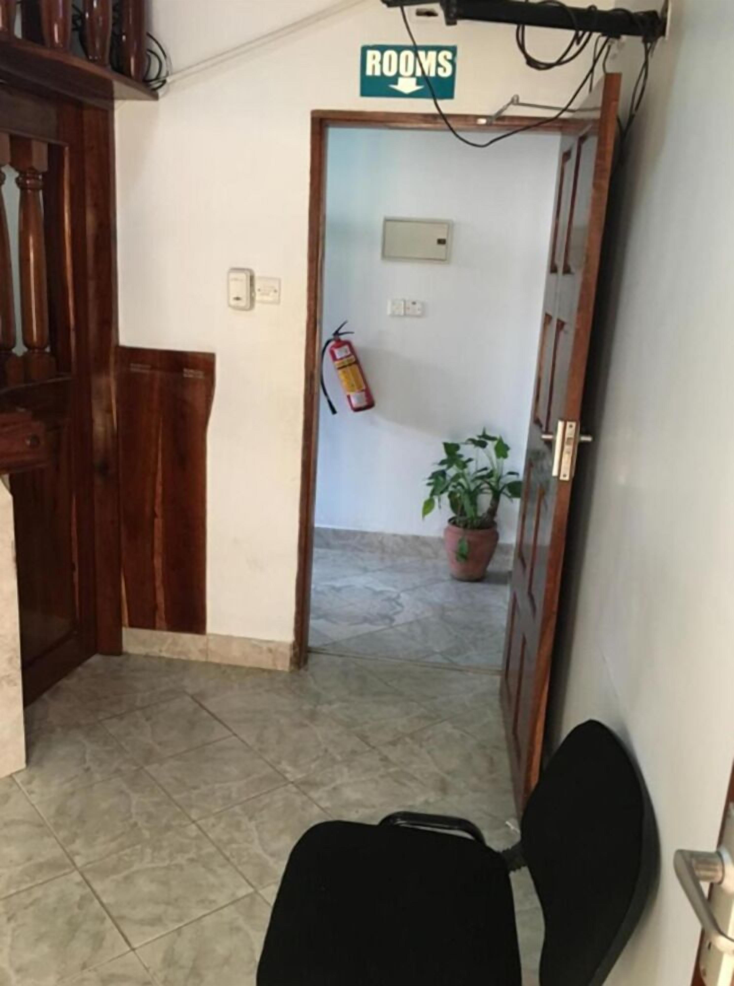 A hallway with a fire extinguisher, a potted plant, and a sign indicating 'ROOMS'.