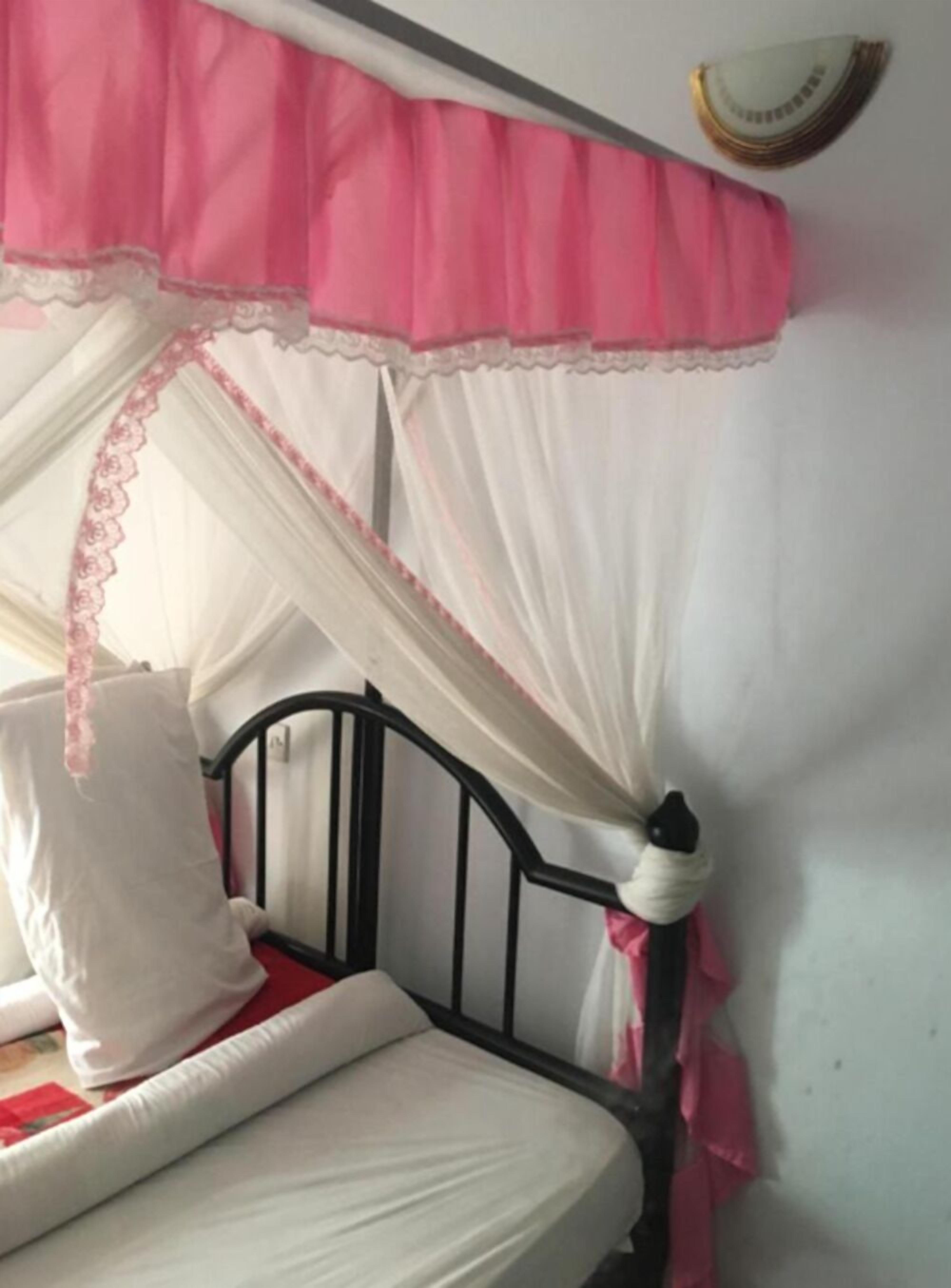 Una cama con estructura de metal negro, ropa de cama blanca y un dosel rosa y blanco.
