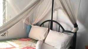 A single bed with a canopy, a floral bedspread, and a plain wall.