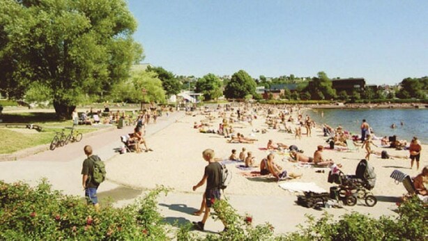 A beach with people sunbathing and swimming, surrounded by greenery and a body of water. - Solferie Holiday Apt. Kronprinsensgate (Kristiansand)