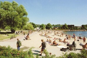 Una playa con gente tomando el sol y nadando, rodeada de vegetación y una extensión de agua.